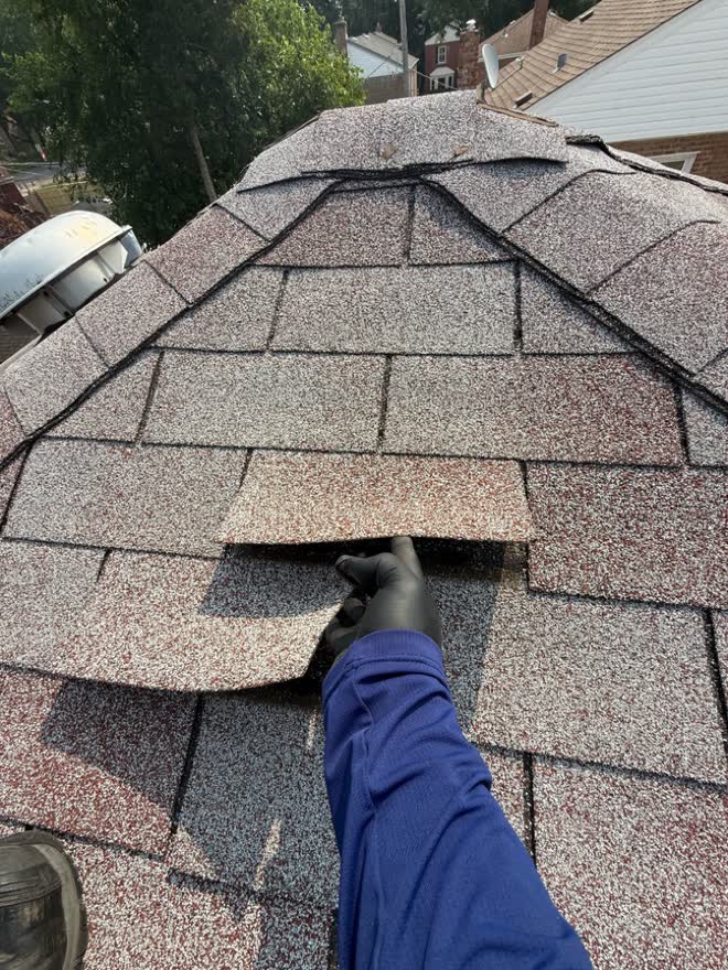 Gloved hand lifting a shingle torn loose by a storm